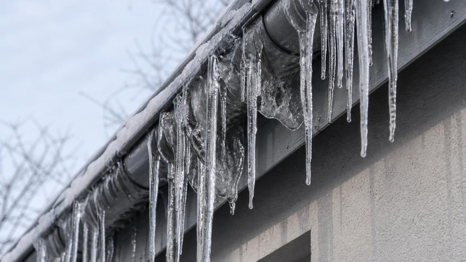 Dachrinne mit langen Eiszapfen und Eisbildung an der Traufe eines Wohnhauses im Winter