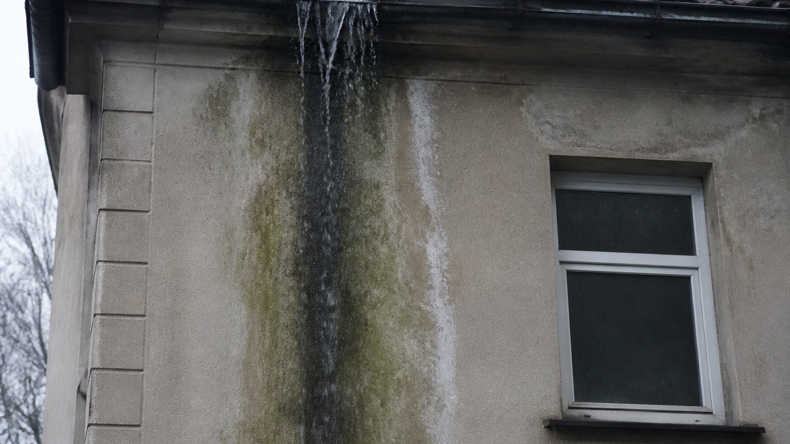Feuchter Streifen an der Fassade unterhalb einer überlaufenden Dachrinne