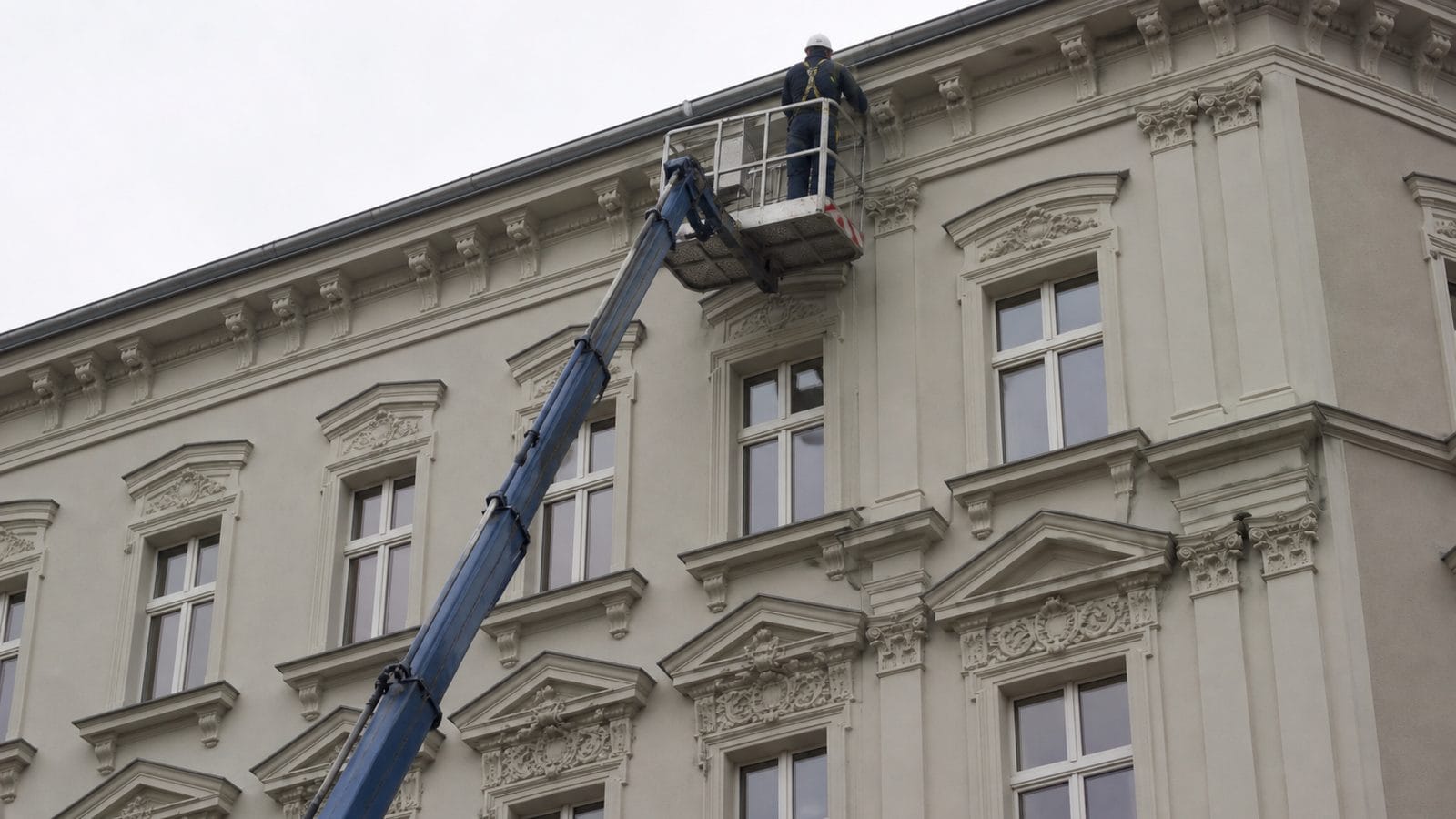 Arbeiter an einer hohen Fassade sichert sich und reinigt die Dachrinne unter dem Dachrand