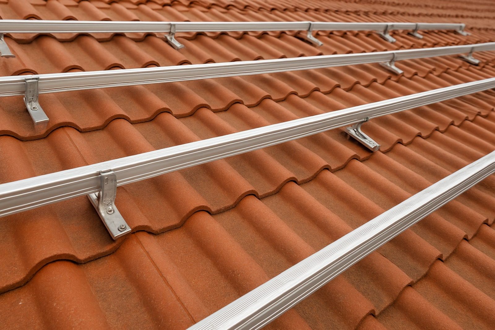 Photovoltaik Solingen: fertig montierte Unterkonstruktion mit silbernen Aluminium-Montageschienen auf Dachhaken auf einem roten Ziegeldach