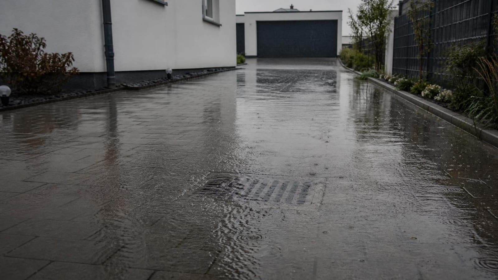 Wasser steht nach Starkregen auf einem gepflasterten Hof vor einem Wohnhaus