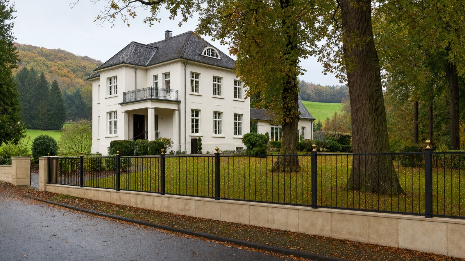Zaunbau Ratingen: schwarzer schmiedeeiserner Stabzaun auf einem hellen Sandstein-Sockel vor einer Villa der 1920er Jahre mit alten Buchen